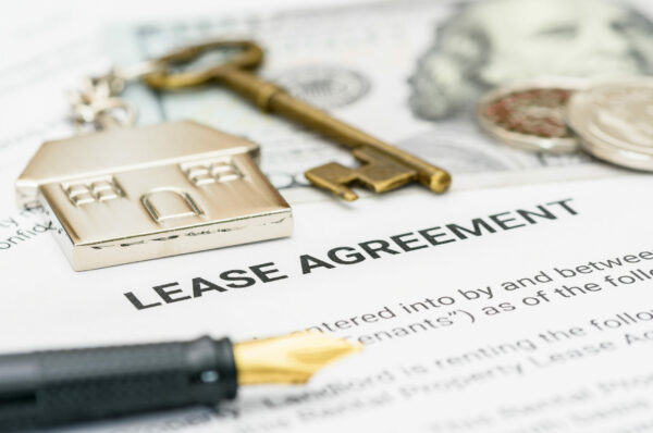 Property rental, leasing contracts, real estate, housing agreements, and property management. A close-up view of a lease agreement document with a house key, coins, US dollar, and a pen placed on top.